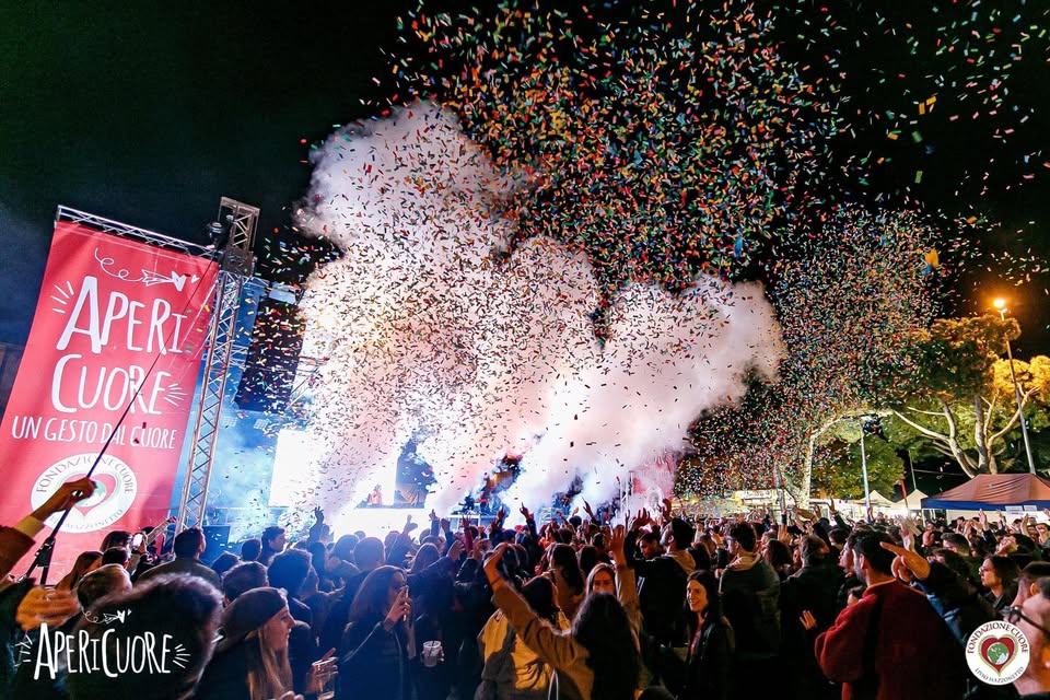 AperiCuore 2026 Potrebbe essere un'immagine raffigurante una o più persone, incendio, fuochi_d'artificio, folla e il seguente testo "ee APERI CUORE UN GESTO UNGESTODALC ODALCUORE DAL CUORE የኢ עחמס APERICUORE 오도 ر _וצובה"